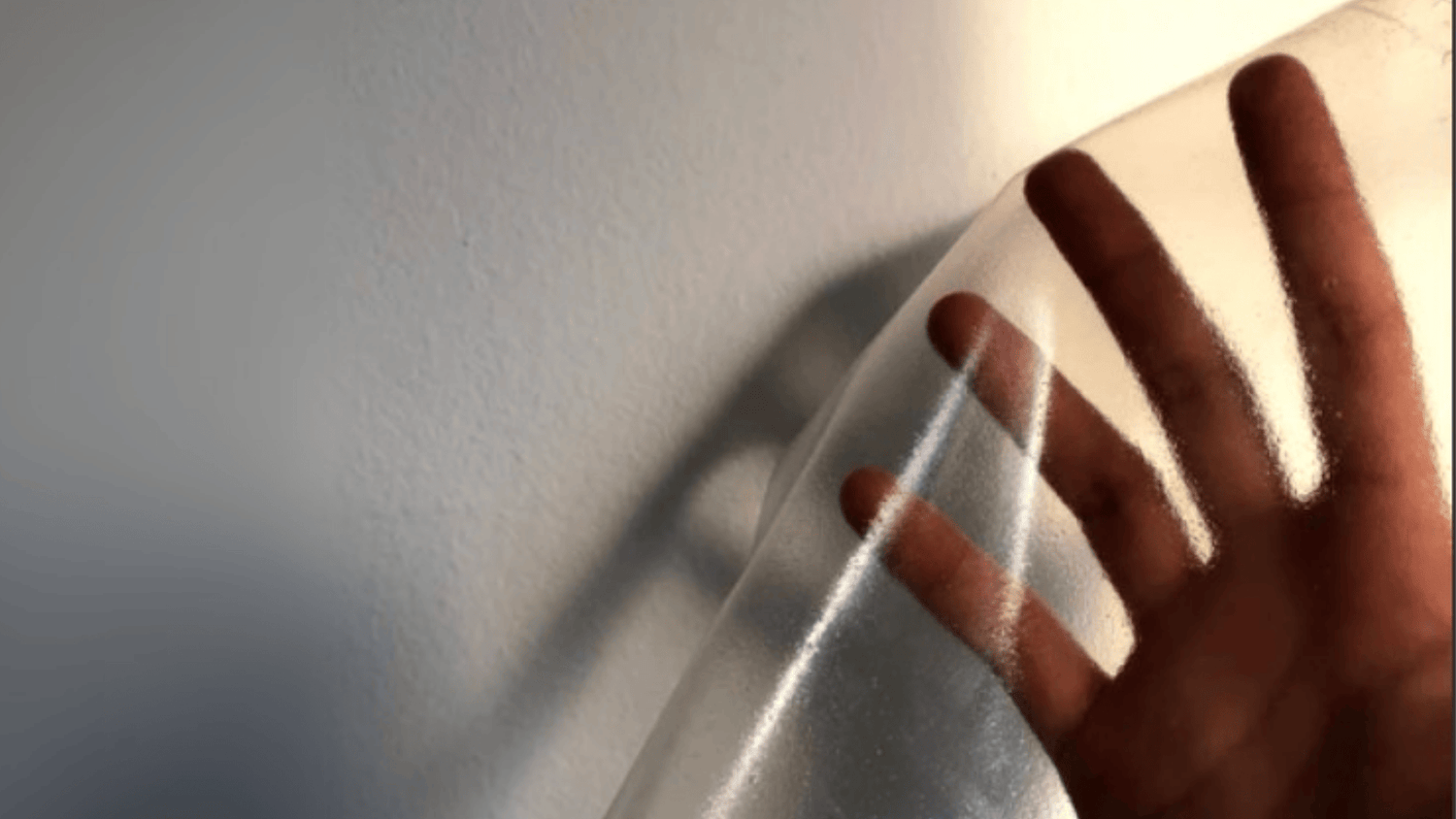 Hand holding a clear plastic sheet against a light gray wall