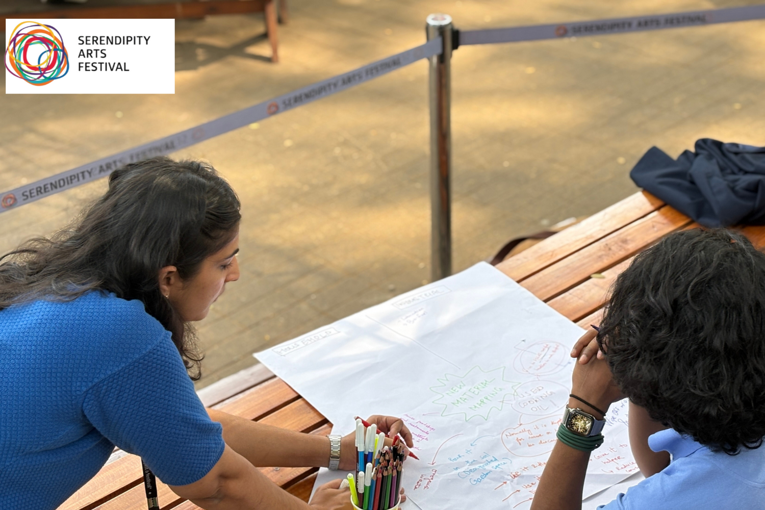 People sitting around a table with a large sheet of paper, possibly for a drawing or planning activity, with a 'Serenity' logo in the corner.