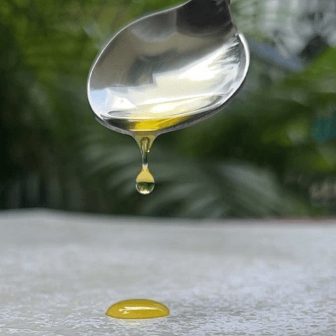 Spoon with a drop of oil dripping onto a white surface with a green blurred background