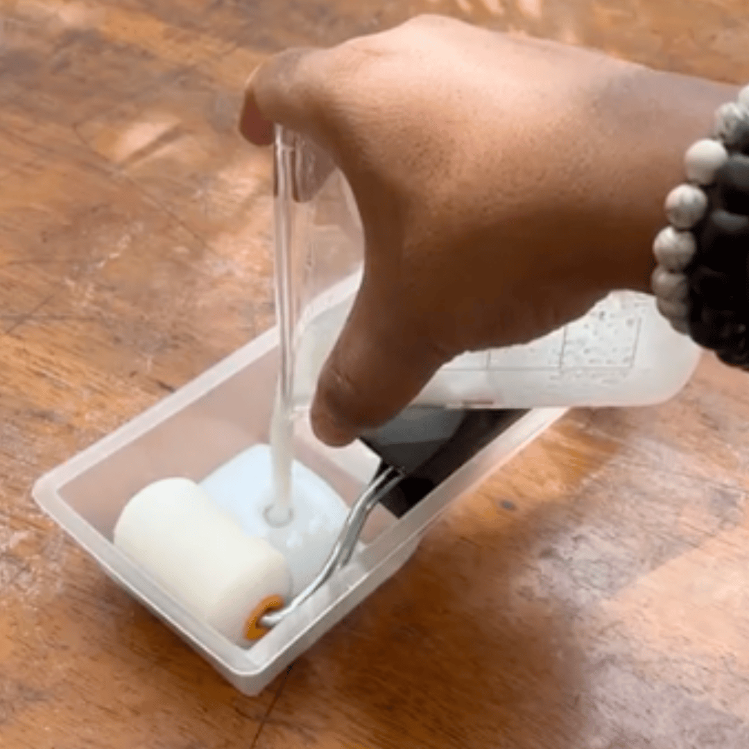 Hand pouring liquid into a container with a white object on a wooden surface